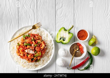 dinde frisées garnies de légumes et sauce tomate surmontée sur riz sur une plaque blanche avec fourchette dorée sur une table en bois avec ingrédients, vie horizontale Banque D'Images