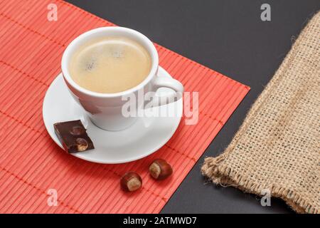 Tasse de café sur la soucoupe avec un morceau de barre de chocolat, noix sur la serviette de bambou et sac en toile de sac sur un fond noir. Vue de dessus. Banque D'Images