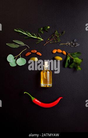 Image visage souriant à faire à partir d'herbes et bouteille d'huile essentielle sur fond noir, vue de dessus, plat Banque D'Images