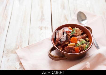 Cassoulet. Contenant des saucisses de porc à la viande, des oies, des canards et parfois des mutons et deux types de haricots blancs. Cuisine française. Sur fond blanc en bois ancien. Banque D'Images