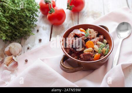 Cassoulet. Contenant des saucisses de porc à la viande, des oies, des canards et parfois des mutons et deux types de haricots blancs. Cuisine française. Sur fond blanc en bois ancien. Banque D'Images