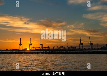 Silhouettes de grues et machines industrielles contre le ciel coloré coucher de soleil sur l'arrière-plan Banque D'Images