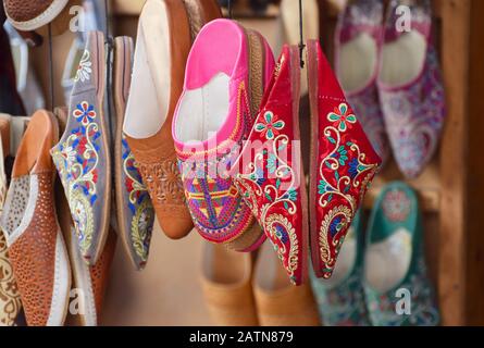 Des chaussons marocains traditionnels brodés aux couleurs vives, appelés pantoufles de babuche accrochées par paires sur un marché dans un souk de Marrakech Banque D'Images