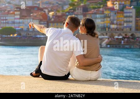 Couple amoureux, hugging, boire du vin et profiter de la vue sur le coucher du soleil à Porto, Portugal. Amoureux de la vue arrière. Panorama de la vieille ville de Porto à la rivière Duoro. Homme poin