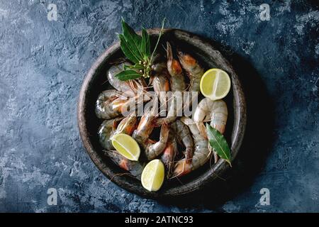 Crevettes non cuites à la crevette avec de la chaux et des herbes en plaque d'argile. Fond en béton foncé. Couche plate, espace de copie Banque D'Images