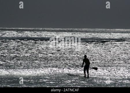 Silhouette d'un surfeur avec la plage étincelante d'argent la nuit Banque D'Images