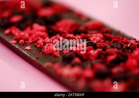 Chocolat hypocalorique noir avec de petits fruits rouges sur fond rose vif, selective focus Banque D'Images