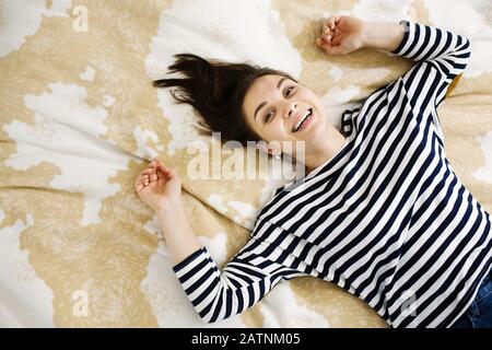 Portrait drôle de jeune femme heureuse et attrayante posée sur un lit, femme riant, vue de dessus, espace pour le texte Banque D'Images