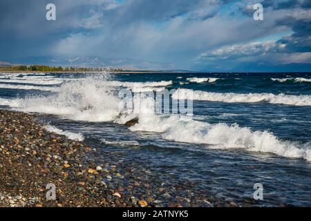 Vagues se brisant sur les rochers et les galets à la plage du Lago Buenos Aires aka Lago General Carrera, Andes montagnes en distance, Patagonia, Argentine Banque D'Images