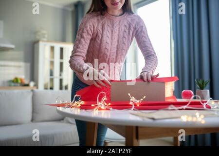 Fille à poil foncé dans une chemise rose couvrant une boîte de cadeau Banque D'Images