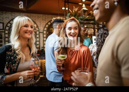 Un groupe d'amis buvant des cocktails dans un bar ensemble. Ils sourit et parlent les uns avec les autres. Banque D'Images