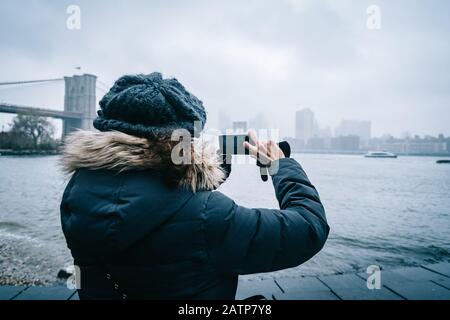 Femme de tourisme avec vêtements chauds prenant une photo de New York Skyline Banque D'Images