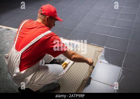 Un travailleur de la construction La mise de nouvelles tuiles de plancher. Banque D'Images