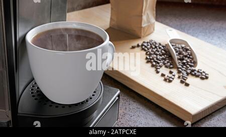 Café fraîchement préparé avec une pelle de grains de café sur planche à découper en bois. Banque D'Images