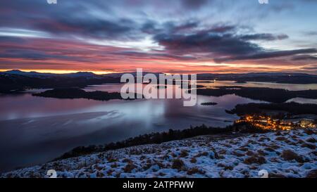 Lever du soleil sur un matin nuageux et hivernal au-dessus du village de Luss et du Loch Lomond, vu des pentes de Beinn Dubh, Écosse. Banque D'Images