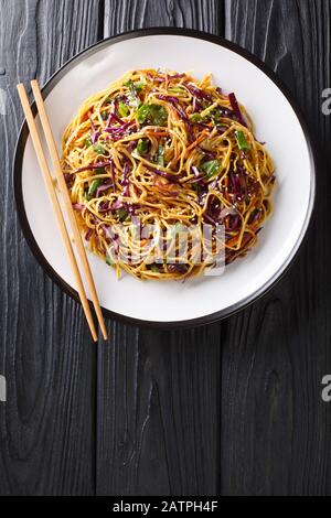 Salade de nouilles asiatiques avec chou rouge émincé, carottes julientées dans une vinaigrette épicée aux arachides dans une assiette sur la table. Vue de dessus verticale de Banque D'Images