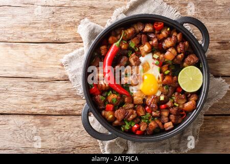 Délicieux plat de sisig philippin servi avec des œufs, de la chaux et du piment dans une poêle sur la table. Vue de dessus horizontale Banque D'Images