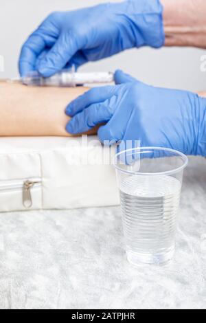 Peur du concept de la procédure d'échantillonnage des tests sanguins avec le médecin qui collecte du sang de la veine du bras d'un patient en arrière-plan et de la tasse en plastique de l'eau au foyer Banque D'Images
