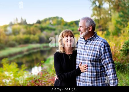 Un couple d'âge mûr qui profite de temps de qualité ensemble tout en marchant le long d'une rivière dans un parc de la ville, lors d'une chaude soirée d'automne; St. Albert, Alberta, Canada Banque D'Images