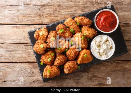Portion de nuggets de poulet frits Dans des flocons de noix de coco servis avec du ketchup et de la mayonnaise près d'une planche en ardoise sur la table. Vue de dessus horizontale fr Banque D'Images