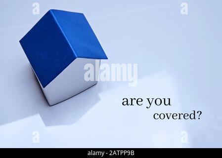 Un modèle d'une maison avec un toit bleu classique se dresse sur une surface brillante. Concept d'assurance immobilière. Inscription Vous êtes couvert. Banque D'Images