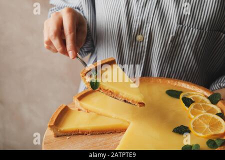 Femme tenant planche en bois et spatule avec tarte au citron sur fond brun, gros plan Banque D'Images