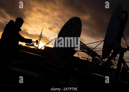 Hambourg, Allemagne. 04 février 2020. Un technicien se tient au coucher du soleil à côté de deux plats satellites sur le toit d'un immeuble de bureaux. Crédit: Christian Charisius/Dpa/Alay Live News Banque D'Images