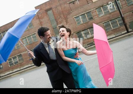 Young couple holding parapluies dans un jour de vent et de rire Banque D'Images