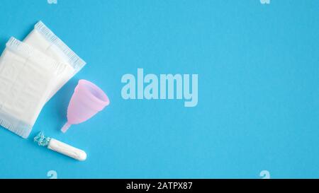 Vue de dessus des produits d'hygiène menstruelle. Coupelle menstruelle plate, tampons hygiéniques, tampon sur fond bleu avec espace de copie. Concept de soins de santé pour les femmes. Banque D'Images