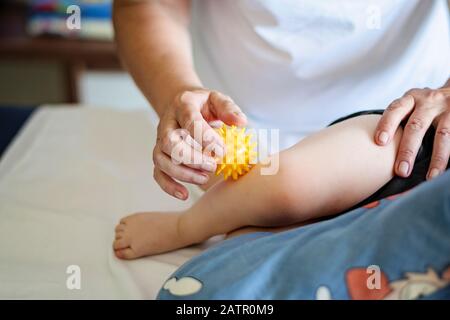 Bébé ayant un massage des pieds dans un centre de réadaptation. Petit enfant en thérapie. Massothérapeute massant un bébé avec ballon de massage jaune. Banque D'Images