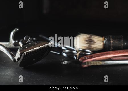 Equipement de salon de coiffure vintage sur fond noir . Outils de coiffure professionnels. Ciseaux, tondeuse à cheveux manuelle, rasoir, brosse de rasage. Minerai horizontal Banque D'Images