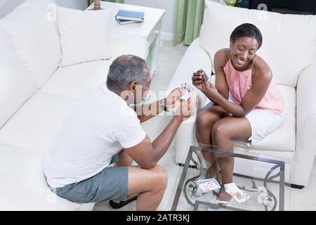 Couple assis dans un salon de cartes à jouer et souriant Banque D'Images