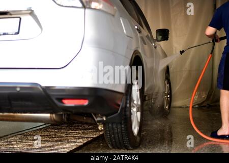 Laver la voiture argentée avec un jet d'eau sous pression du tuyau qui fonctionne à la main. Banque D'Images