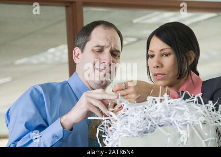 Homme d'affaires et femme d'affaires regardant des documents déchiquetés et essayant de récupérer les informations des shreds Banque D'Images