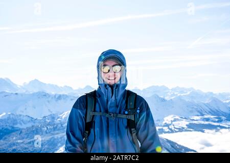 routard mountaineer souriant au sommet contre les couches de montagne enneigées bleues en hiver. ciel ensoleillé et bleu Banque D'Images