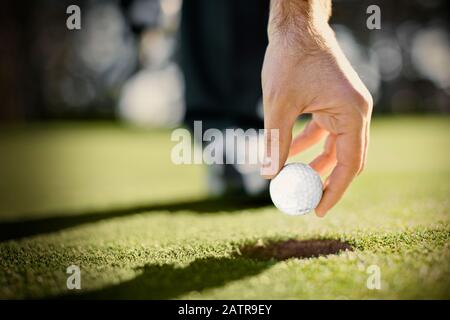 Main tenant une balle de golf au-dessus d'un trou sur un terrain de golf. Banque D'Images