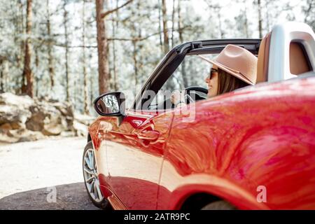 Femme conduisant une voiture rouge convertible en voyageant dans la nature, vue de l'arrière-plan de la voiture avec paysage forestier sur l'arrière-plan Banque D'Images