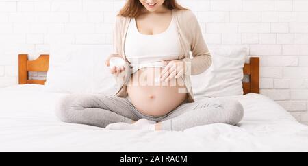Femme enceinte hydratant son ventre avec lotion, panorama Banque D'Images