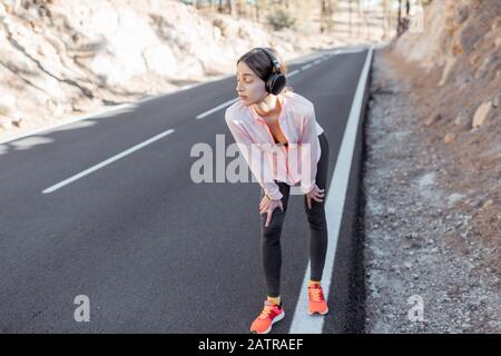 Jeune femme dans les vêtements de sport s'étendant sur la belle route, l'entraînement à l'extérieur dans les montagnes Banque D'Images