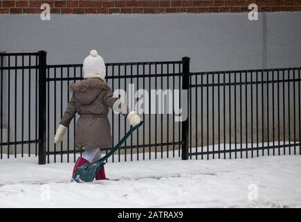 15 janvier 2020 - Montréal, Québec, Canada : jeune fille marchant sur un trottoir en neige avec une pelle le long d'un bâtiment en hiver, dans l'arrondissement de Rosemont Banque D'Images