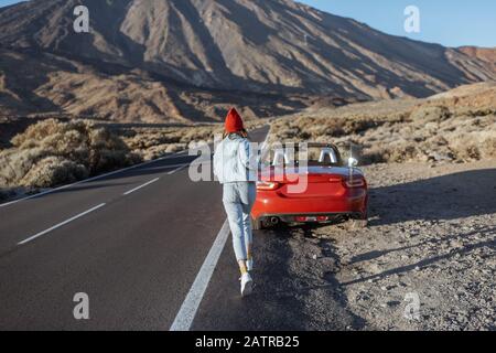 Jeune femme profitant d'un voyage sur route au coucher du soleil, en courant jusqu'à la voiture sur le bord de la route de la belle vallée volcanique. Voyager sur l'île de Tenerife Banque D'Images