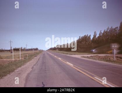 Photographie vernaculaire prise sur un film analogique de 35 mm transparent, considérée comme représentant une route d'asphalte grise sous le ciel bleu pendant la journée, 1965. Les principaux sujets/objets détectés sont la route, le ciel, l'asphalte, l'autoroute, l'horizon, l'arbre, le paysage, la rue et la nature. () Banque D'Images