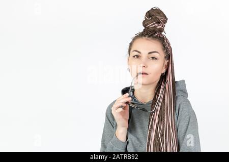 Une belle fille aux queues roses d'afro ou de zizi regarde soigneusement l'appareil photo et tient des lunettes dans ses mains sur un fond blanc avec place pour Banque D'Images