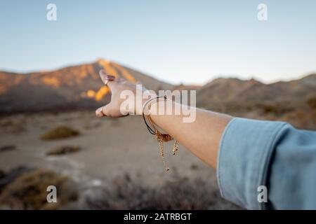 Femme pointant à la main sur la montagne volcanique pendant un coucher de soleil, gros plan sur la main Banque D'Images
