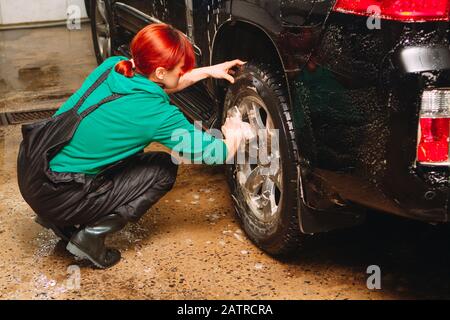 Un employé du lavage de voiture se lave soigneusement effectue le décollement et applique un équipement de protection au corps d'une voiture chère Banque D'Images