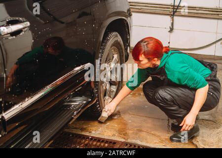 Un employé du lavage de voiture se lave soigneusement effectue le décollement et applique un équipement de protection au corps d'une voiture chère Banque D'Images