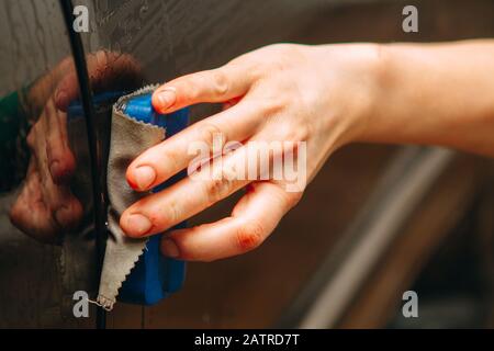 Un employé du lavage de voiture se lave soigneusement effectue le décollement et applique un équipement de protection au corps d'une voiture chère Banque D'Images