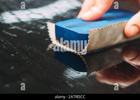 Un employé du lavage de voiture se lave soigneusement effectue le décollement et applique un équipement de protection au corps d'une voiture chère Banque D'Images