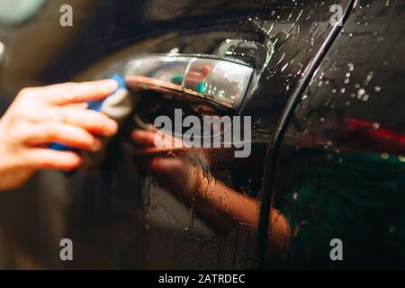 Un employé du lavage de voiture se lave soigneusement effectue le décollement et applique un équipement de protection au corps d'une voiture chère Banque D'Images