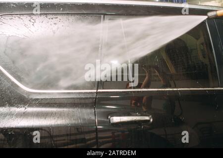 Un employé du lavage de voiture se lave soigneusement effectue le décollement et applique un équipement de protection au corps d'une voiture chère Banque D'Images